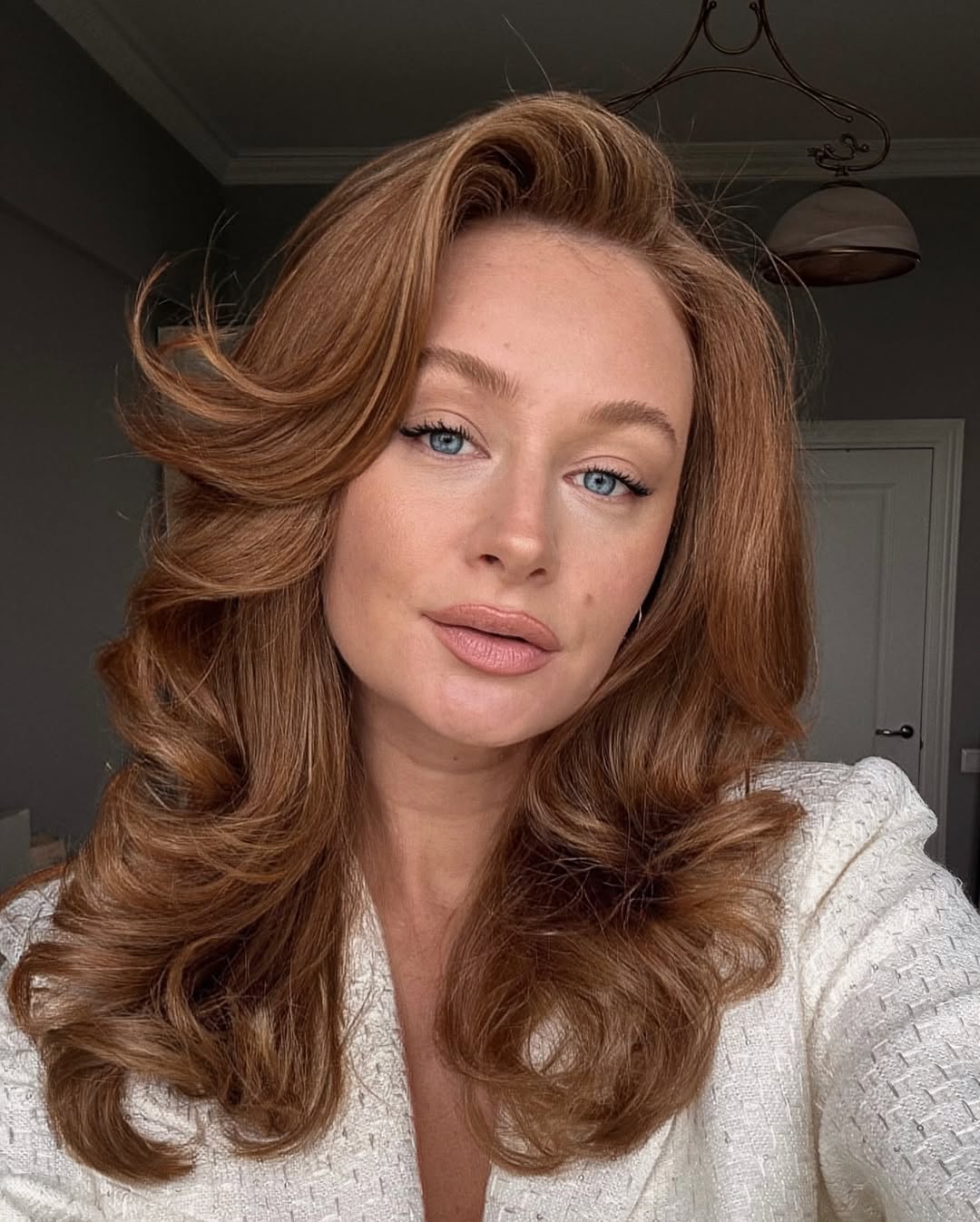 Close-up of a woman with an effortless summer hairstyle 2026, featuring loose waves and a braided section, outdoors in dappled sunlight.
