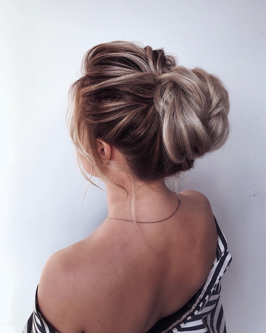 A woman with a chic, messy low bun, perfect for achieving effortless summer hairstyles 2026. She wears a casual white linen top and delicate gold jewelry, ideal for a relaxed daytime look.