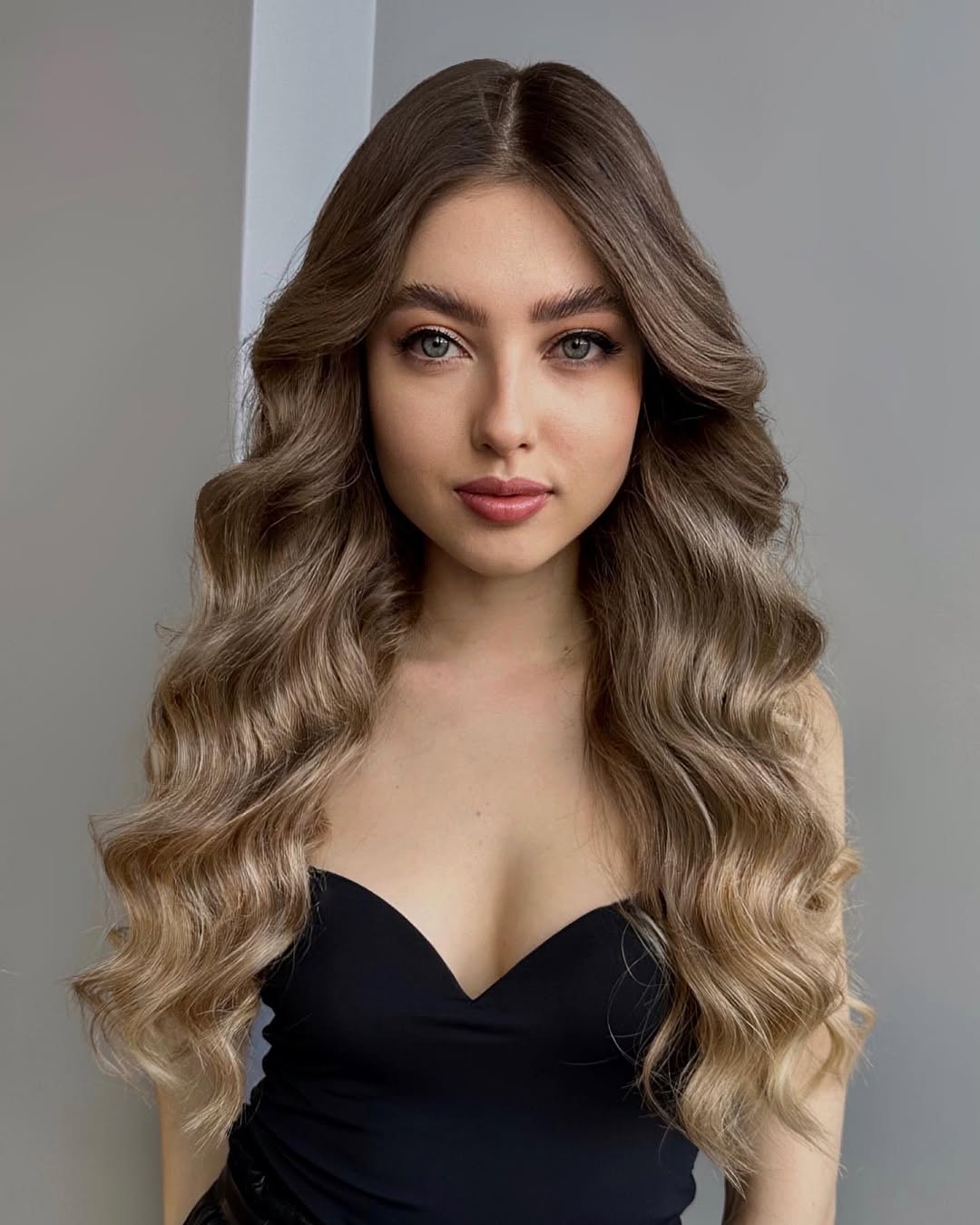 Woman with long, wavy blonde hair in an effortless summer hairstyle, wearing a white off-the-shoulder top and denim jeans outdoors on a sunny day, showcasing a perfect casual look.