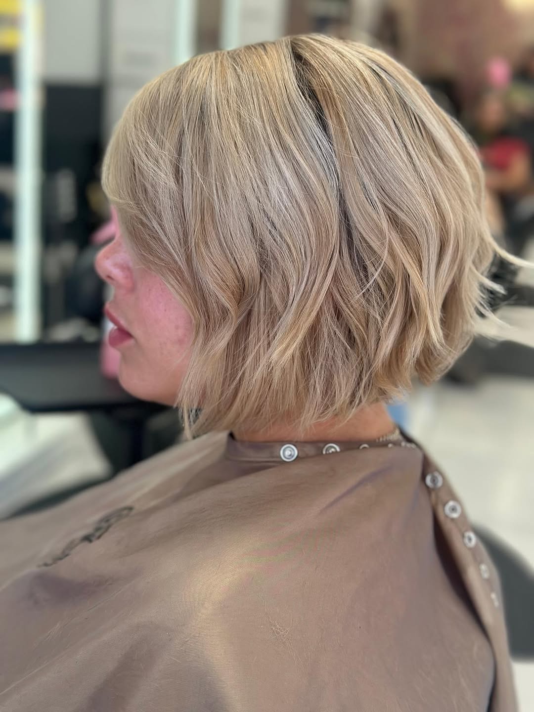Woman with a chic, shoulder-length bob haircut, perfect for flattering summer haircuts 2026. Her light brown hair has subtle highlights, styled in soft waves framing her face. She's wearing a casual white top, suitable for everyday summer outings.