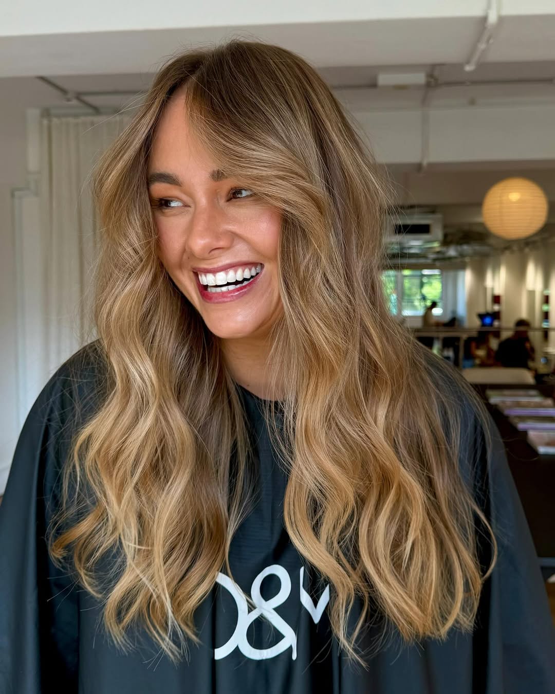Close-up of a woman with vibrant golden balayage summer 2026 hair, styled in soft waves, complemented by a chic cream off-the-shoulder top and natural makeup for a sophisticated, sunny look.