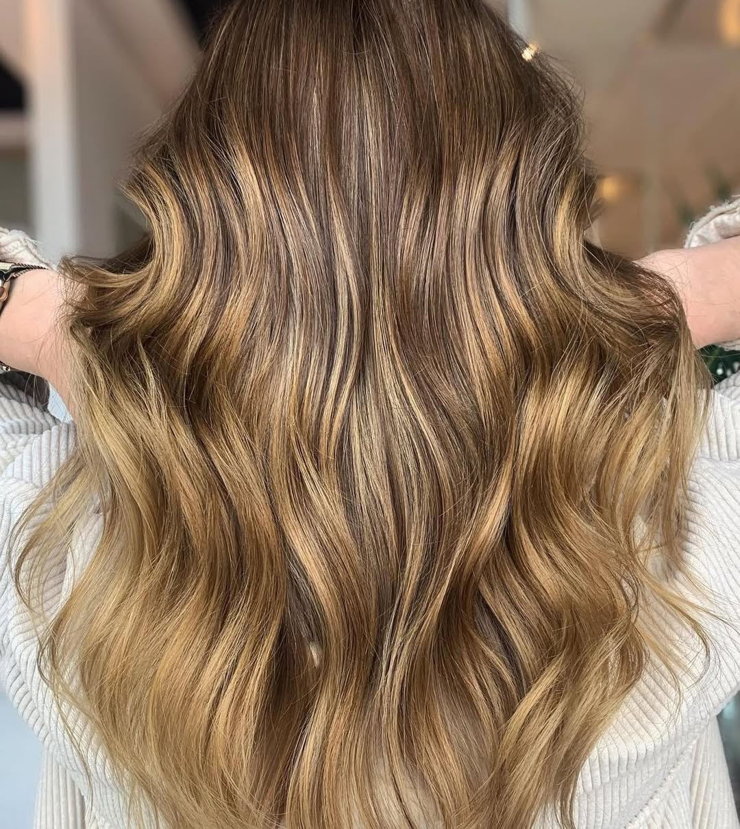 Close-up of a woman with vibrant golden balayage summer 2026 hair, styled in loose waves, wearing a summery white off-shoulder top.