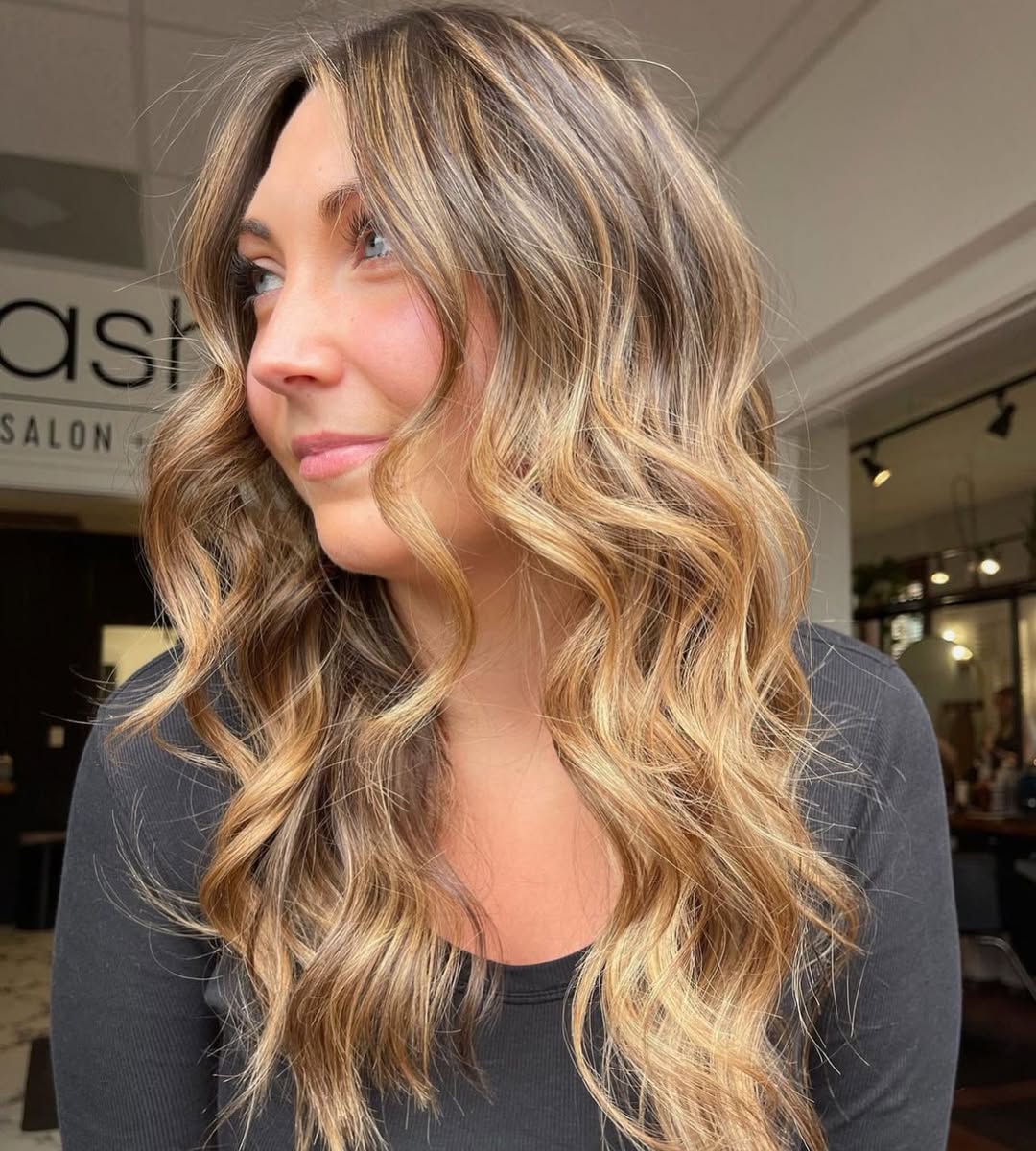 Close-up of a woman with stunning golden balayage summer 2026 hair, styled in soft waves, perfectly complementing a bright white linen dress for a breezy, elegant summer look.