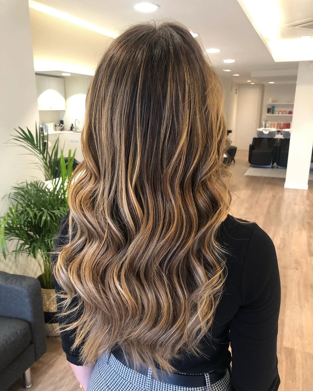 Woman with golden balayage summer 2026 hair wearing a white ruffled top and blue jeans, smiling outdoors.