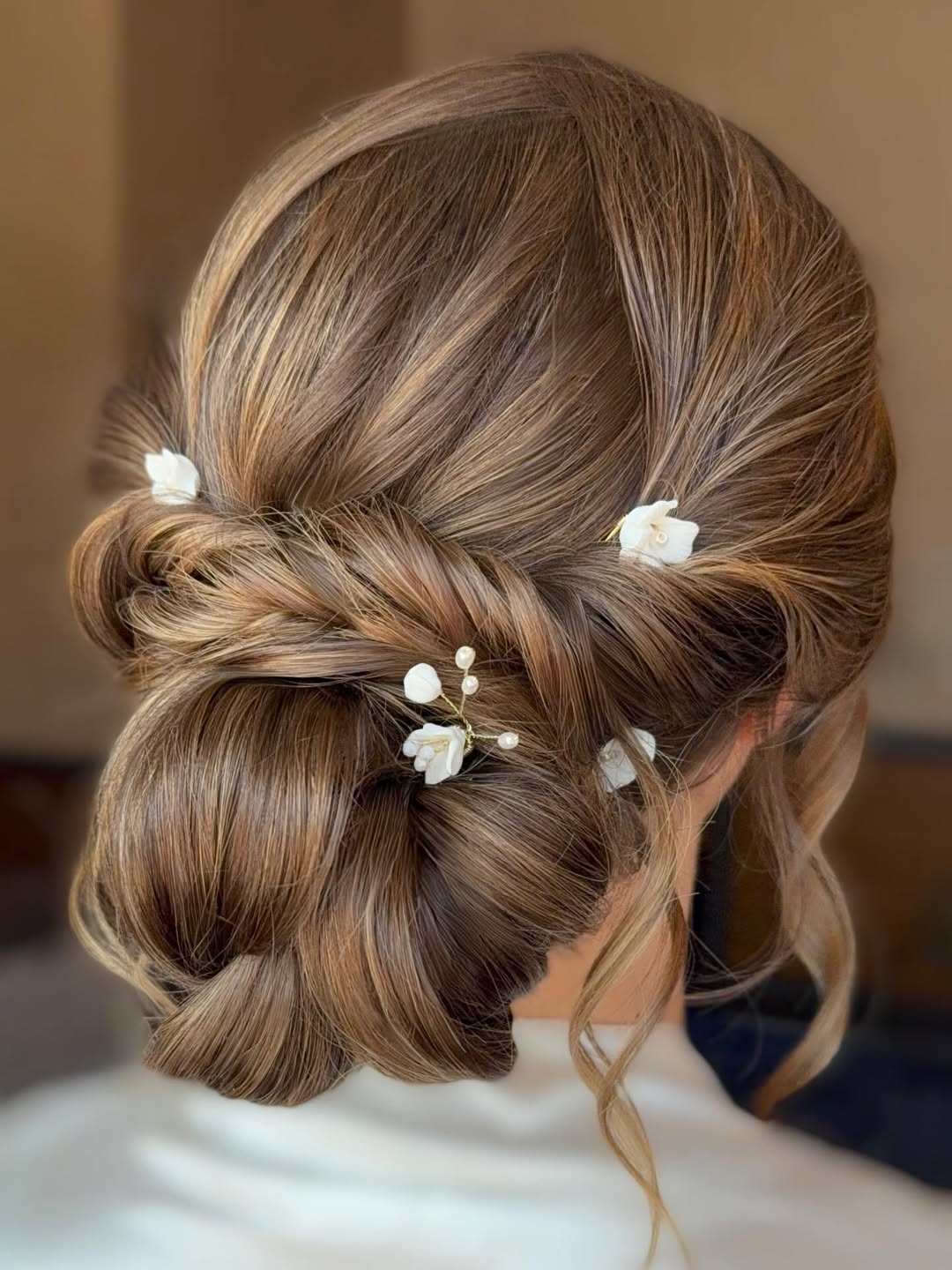 Beautiful blonde woman with a voluminous, half-up braided hairstyle adorned with delicate white flowers, perfect for an outdoor wedding hair summer 2026. The look is elegant and whimsical.