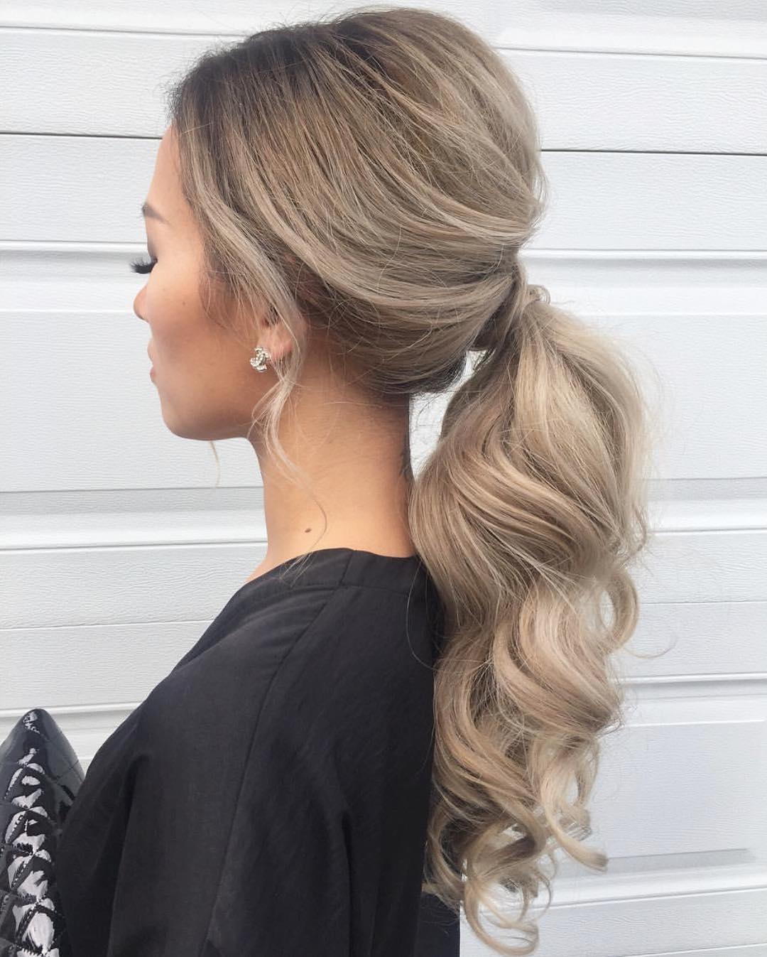 Elegant brunette bride with a cascading, loose braid adorned with white floral accents, perfect for an outdoor wedding hair summer 2026. Her hair is artfully styled to complement an open-back wedding gown.