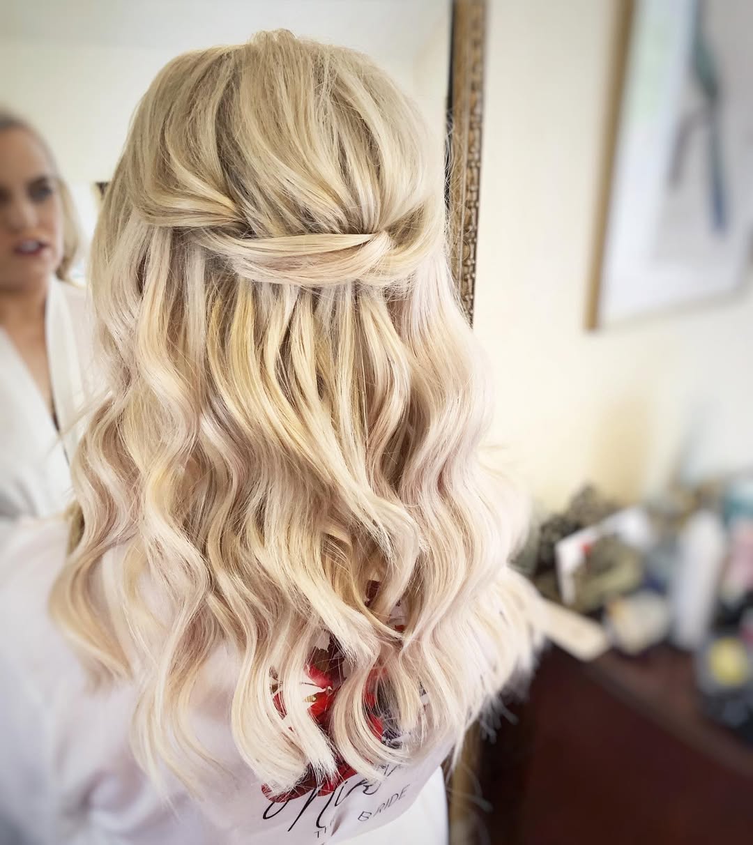 Beautiful blonde woman with a soft, romantic updo, perfect for outdoor wedding hair summer 2026. Her hair features loose curls framing her face, adorned with delicate white floral accessories, complementing a light, airy dress.