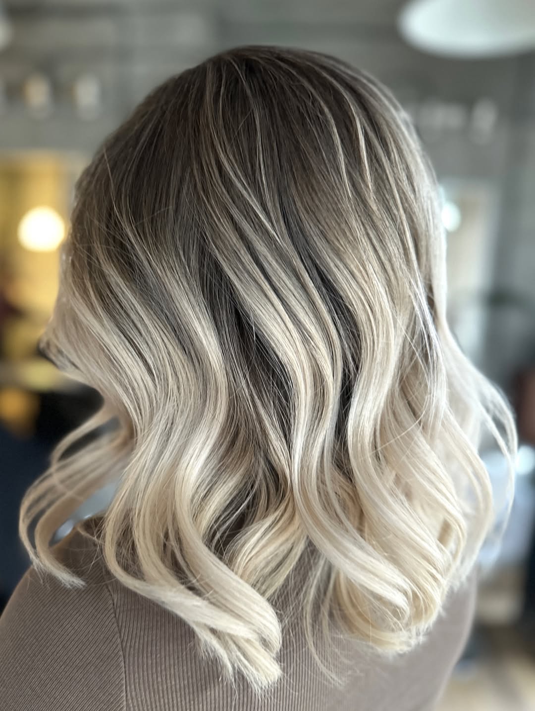Close-up of a woman's hair with natural looking summer babylights balayage 2026, featuring golden blonde highlights against a light brown base.
