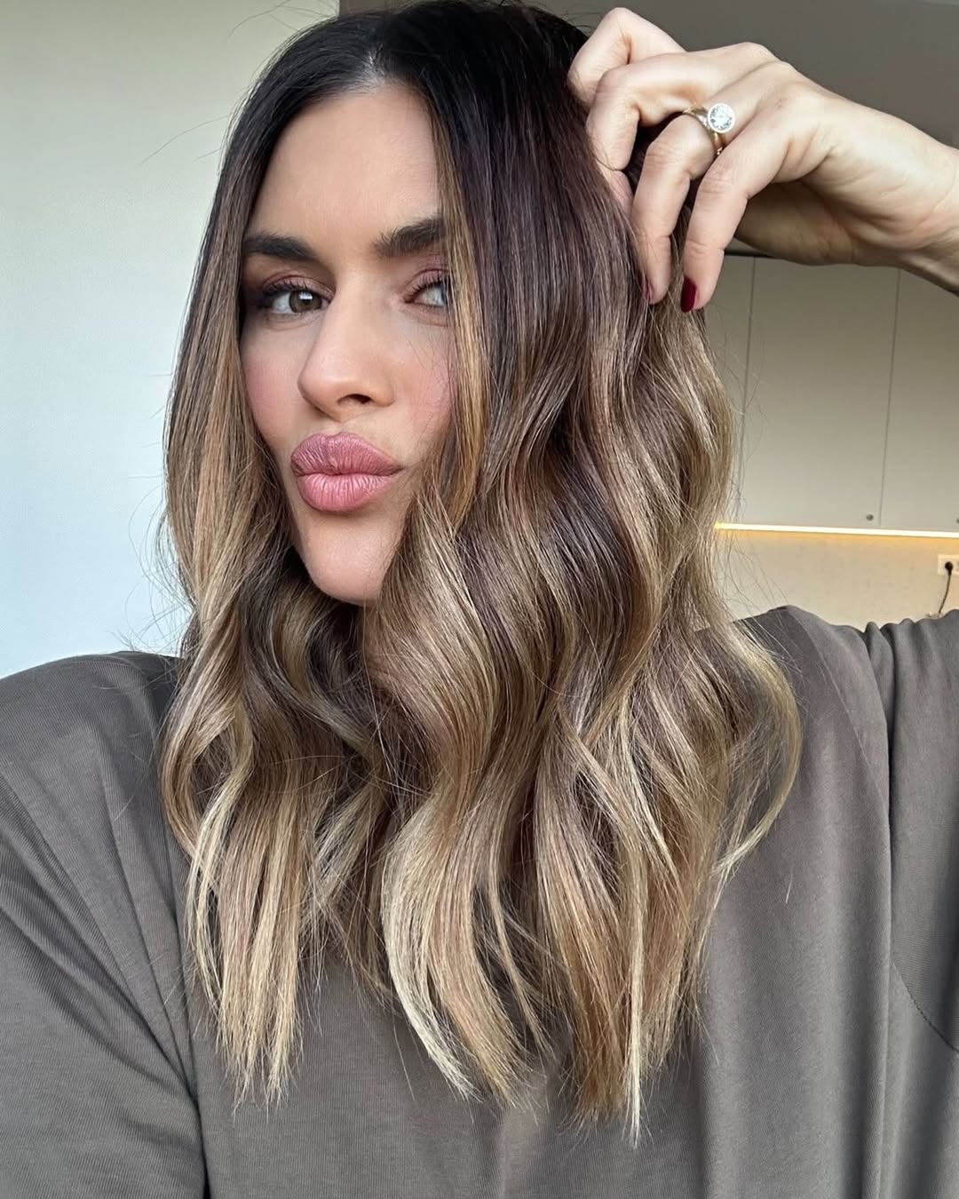 Close-up of a woman smiling, showcasing her blonde hair with subtle summer babylights balayage 2026. Her hair is styled in loose waves, framing her face and highlighting the bright, sun-kissed effect.