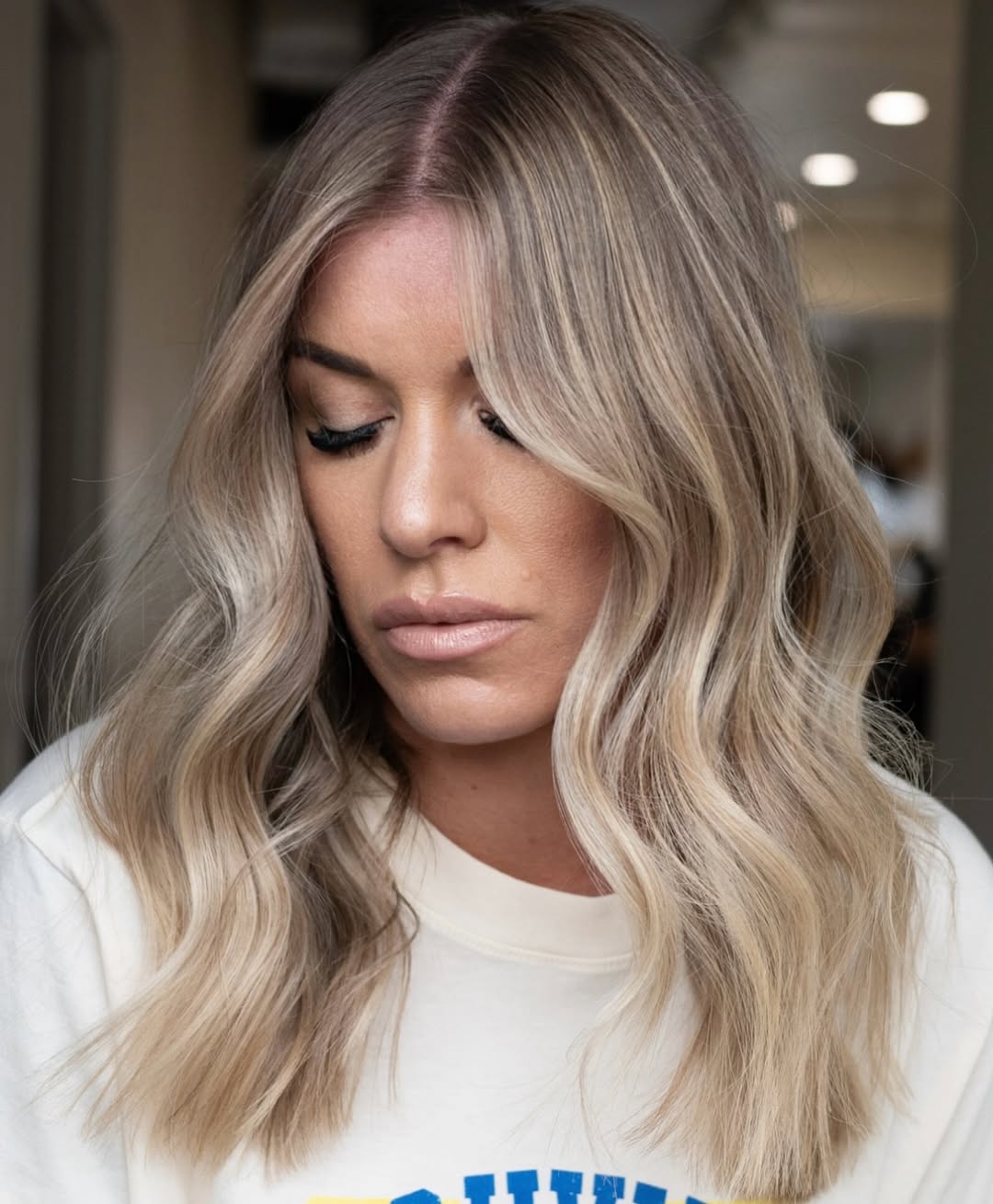 Woman with long, wavy blonde hair showcasing delicate summer babylights balayage. Her hair features a natural blend of light blonde highlights and warmer undertones, perfect for a sun-kissed look.