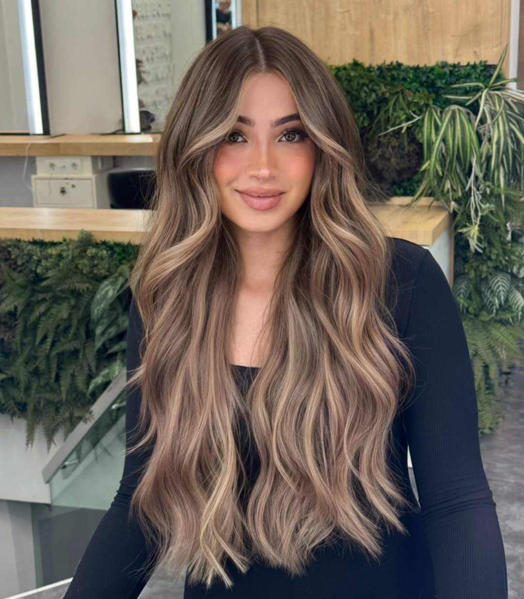 Woman with long, wavy blonde hair showcasing summery babylights balayage. Her hair features a seamless blend of bright blonde and subtle warm tones, ideal for a sun-kissed look.