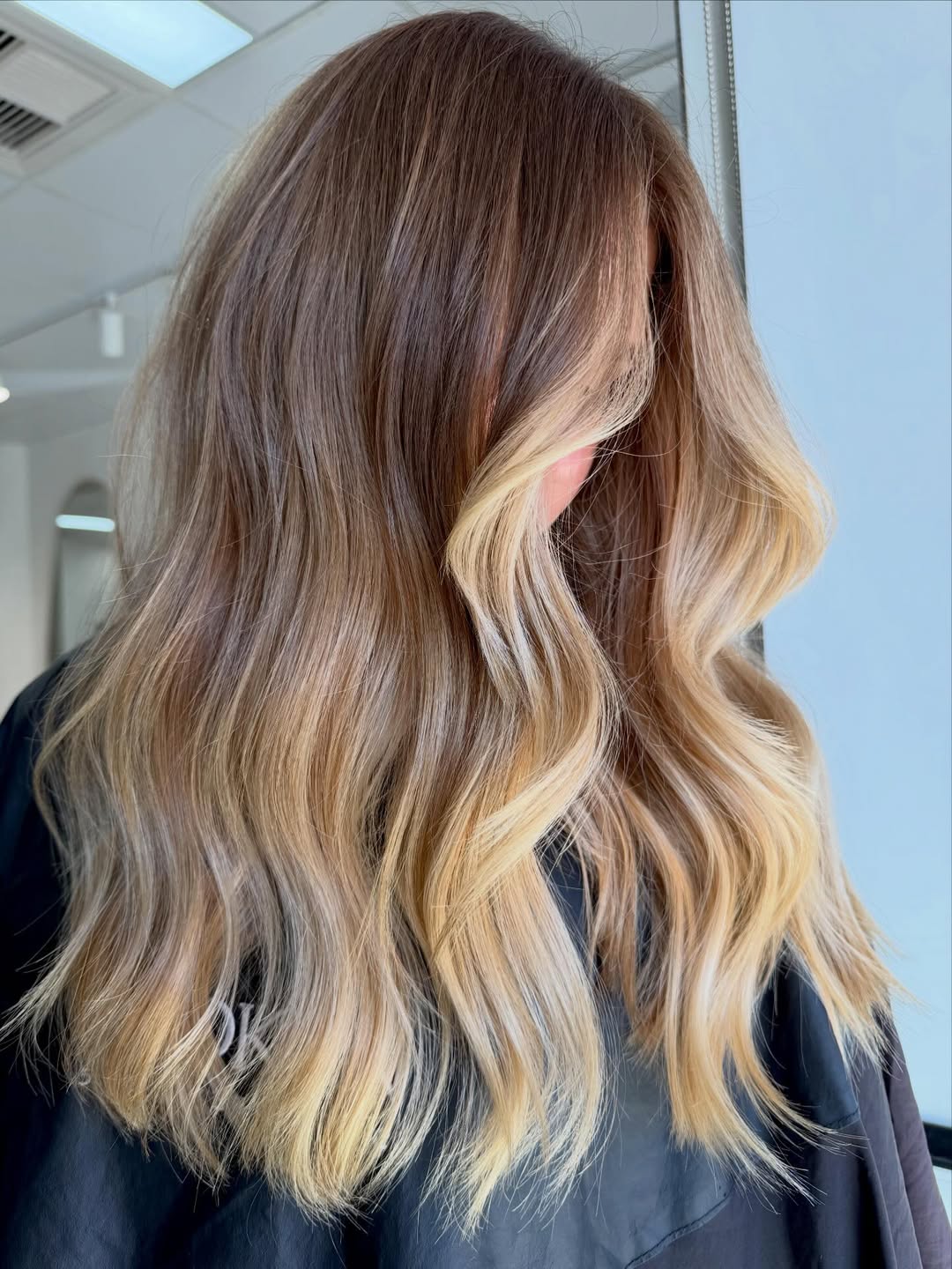 Close-up of a woman's long, wavy brown hair with perfectly blended summer babylights balayage 2026, showcasing sun-kissed blonde highlights and healthy shine.
