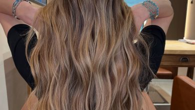 Woman with long wavy hair featuring sun-kissed summer babylights balayage, glowing softly against a blurred outdoor backdrop.