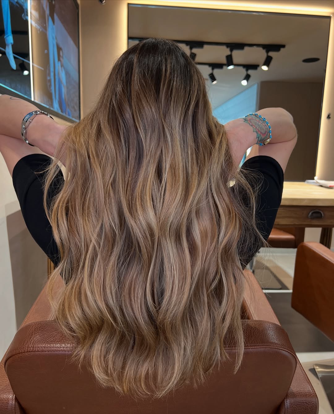 Woman with long wavy hair featuring sun-kissed summer babylights balayage, glowing softly against a blurred outdoor backdrop.