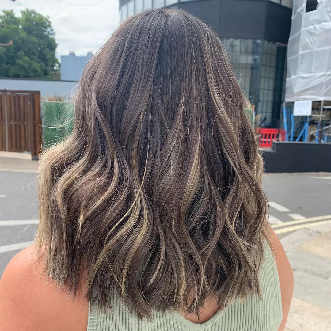 Close-up of a woman with vibrant, sun-kissed blonde hair, ideal for summer hair color options 2026. Her hair has subtle golden highlights and a natural, wavy texture, perfect for a beach vacation.