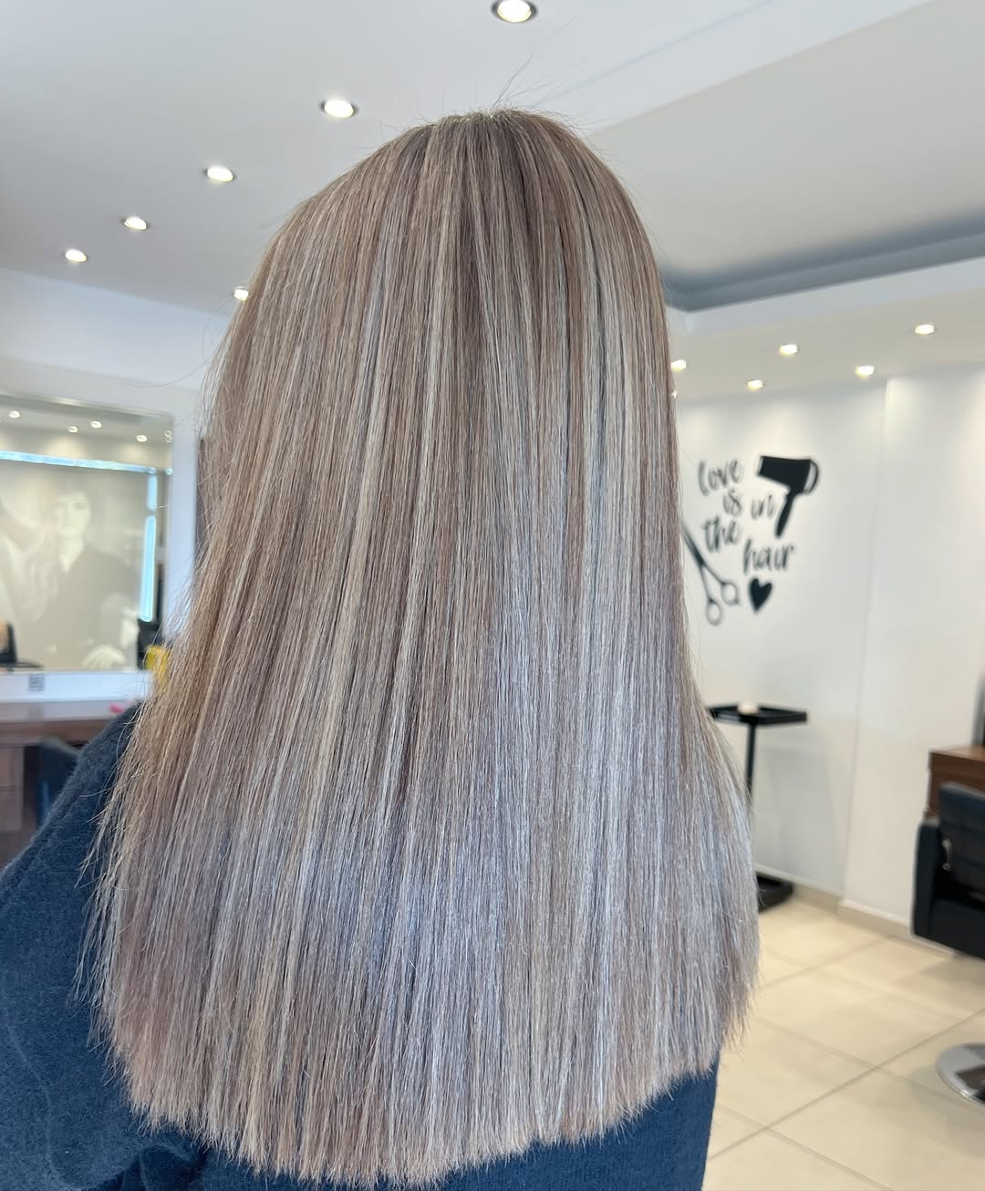 A woman with vibrant blonde hair styled in loose beach waves, perfect for summer hair ideas for blondes. She's wearing a casual white off-the-shoulder top, showcasing a relaxed, sunny vibe.