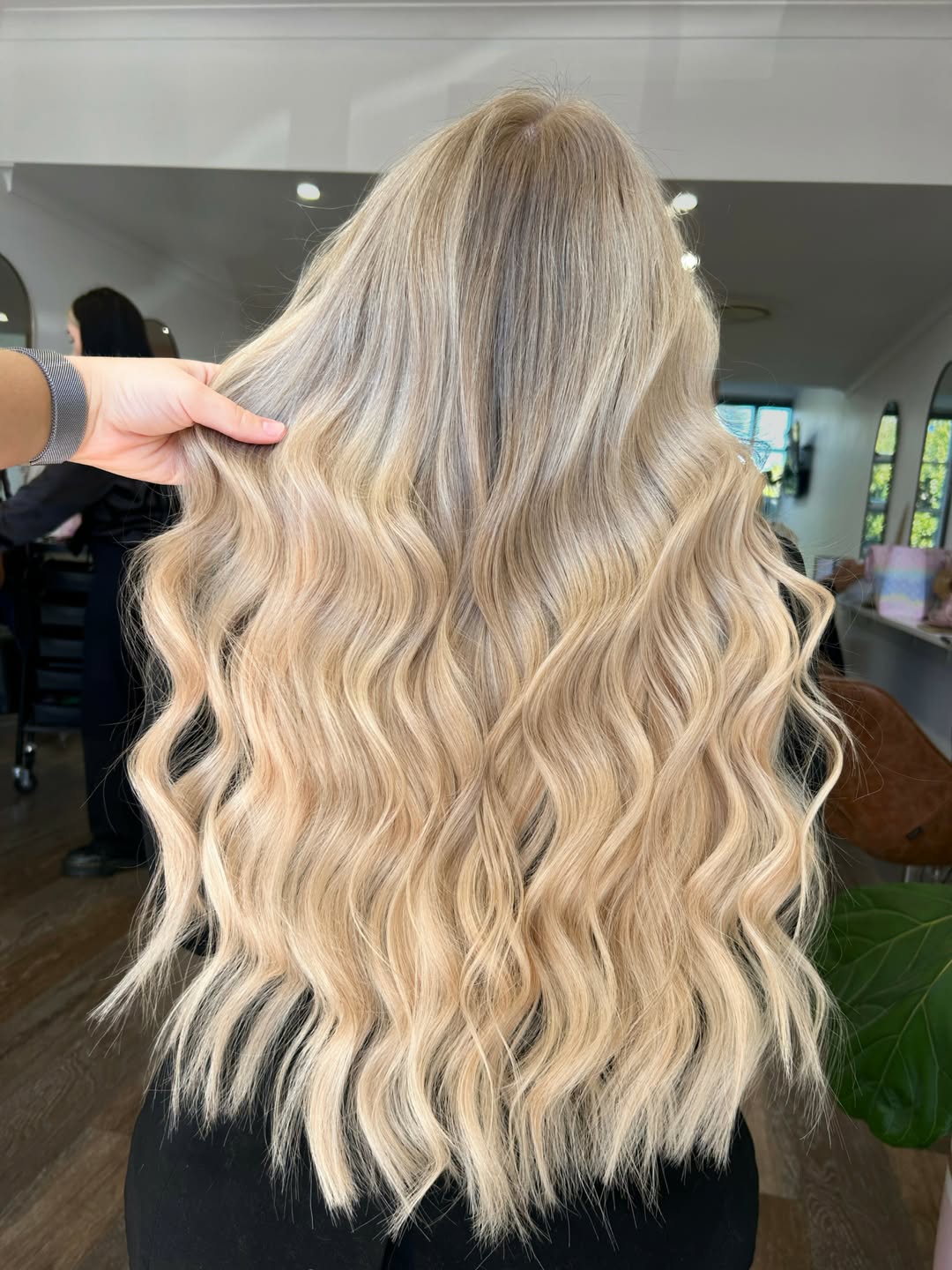 Blonde woman with naturally highlighted waves, a perfect summer hair idea for blondes, smiling outdoors in bright sunlight, showcasing healthy, sun-kissed locks.