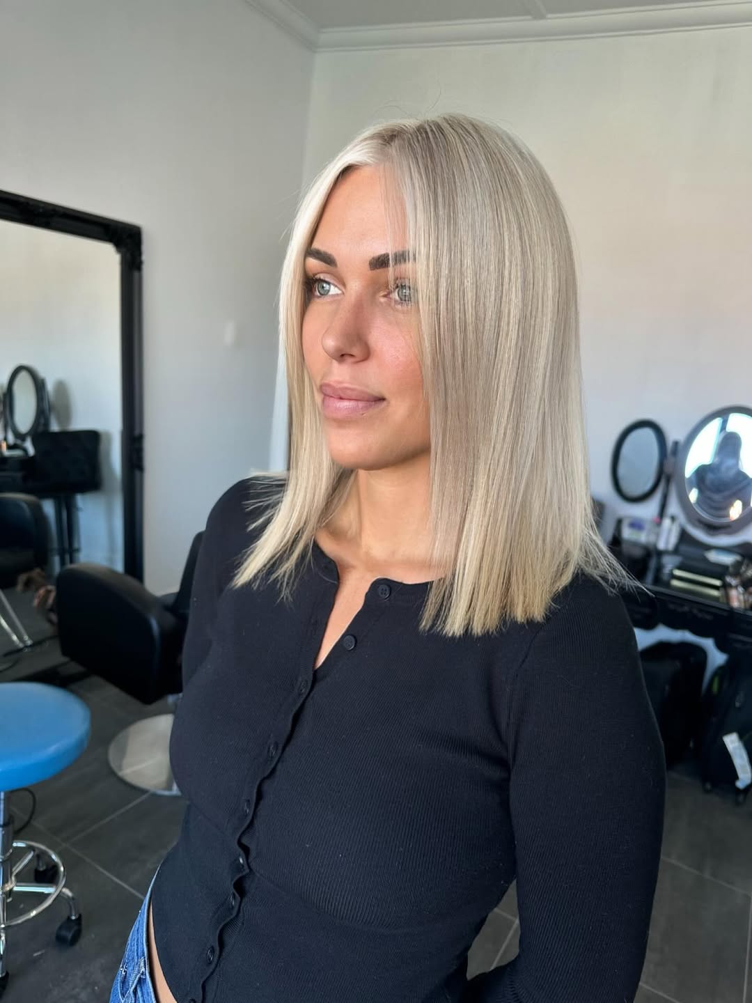 Blonde woman with long, sun-kissed waves, perfect for summer hair ideas for blondes. She's wearing a light floral dress, enjoying a sunny outdoor setting.