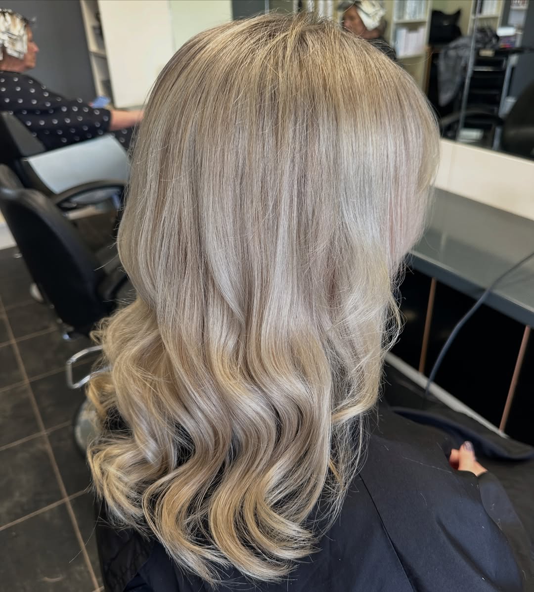 Close-up of a blonde woman with wavy, sun-kissed hair, showcasing light brown roots and expertly blended golden highlights, perfect for summer hair ideas for blondes. Her hair falls loosely around her shoulders, complementing a light, airy summer top.