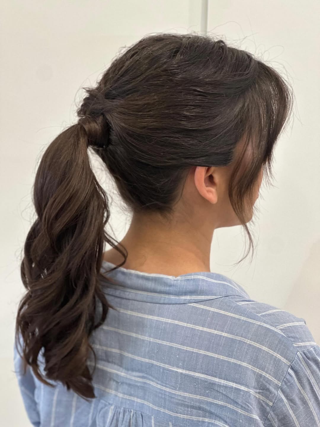 A woman with perfect top summer hairstyles 2026, sporting a chic messy bun with face-framing tendrils, wearing a light blue off-the-shoulder top for a casual sunny day. The style is ideal for warm weather.