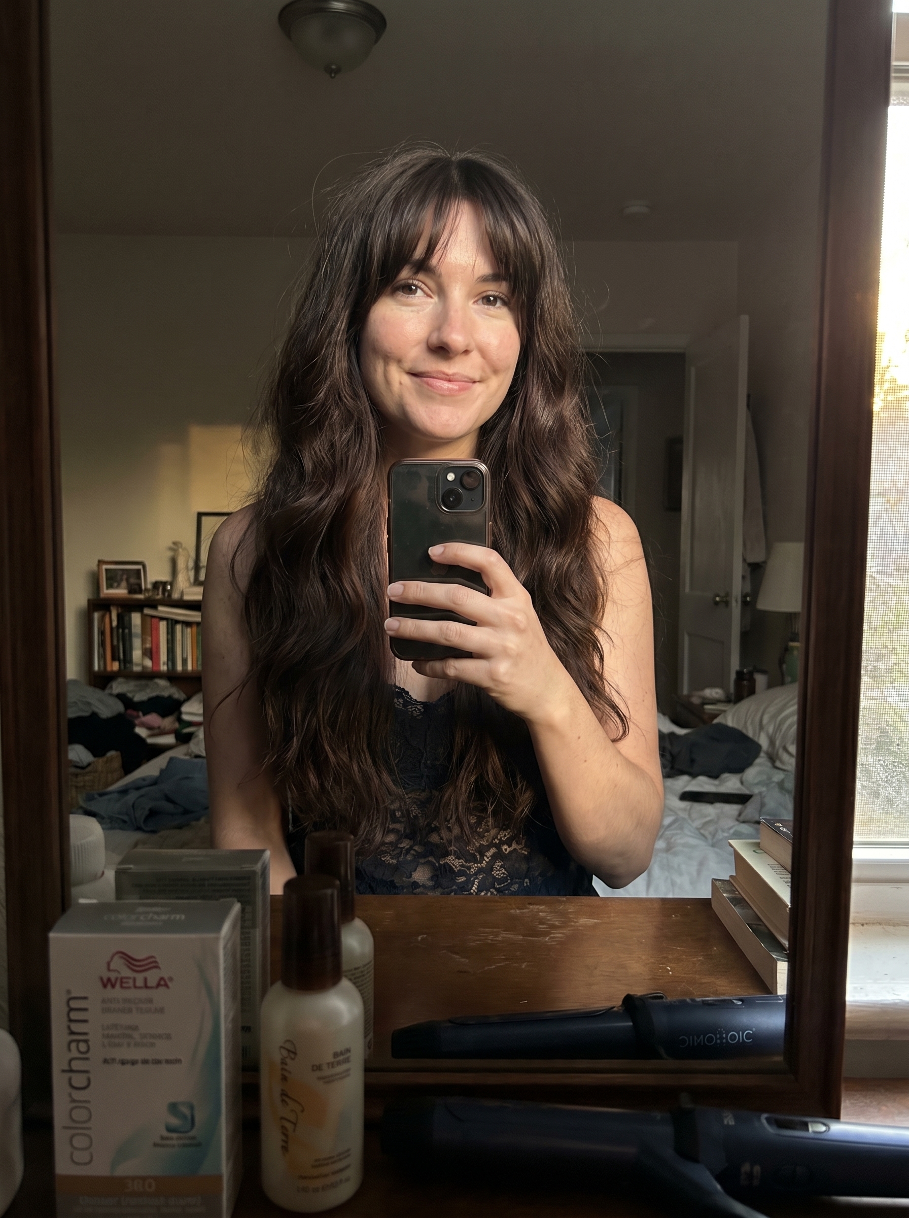 A brunette model with 'Soft Goth Velvet Waves with Wispy Bangs', a trendy haircut for summer 2026. This romantic, edgy style features deep brunette waves created with a large barrel curling iron, complemented by wispy bangs and a velvet-finish styling cream. Perfect for a mysterious date night or evening event.