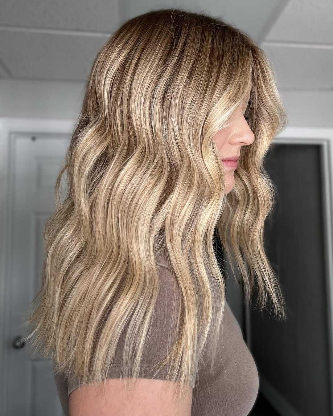 A woman with stunning warm blonde hair for summer 2026, styled in soft waves, wearing a chic white linen top and denim shorts, perfect for a sunny day out.