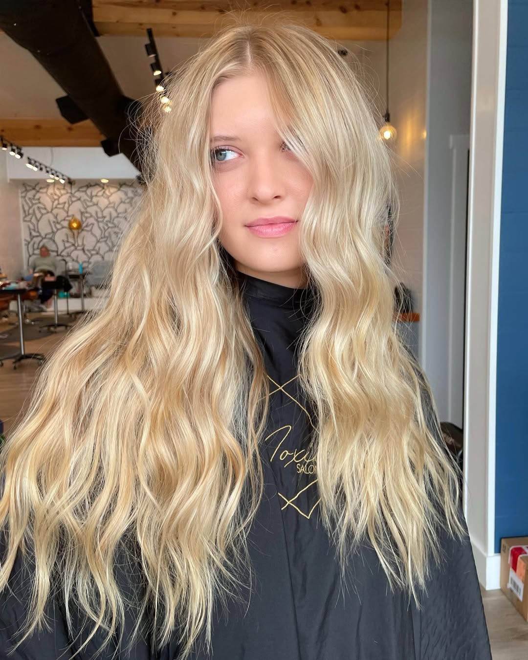 Woman with luscious warm blonde hair, styled in loose waves, wearing a chic white off-the-shoulder top for a perfect summer 2026 look. Ideal for casual outings.