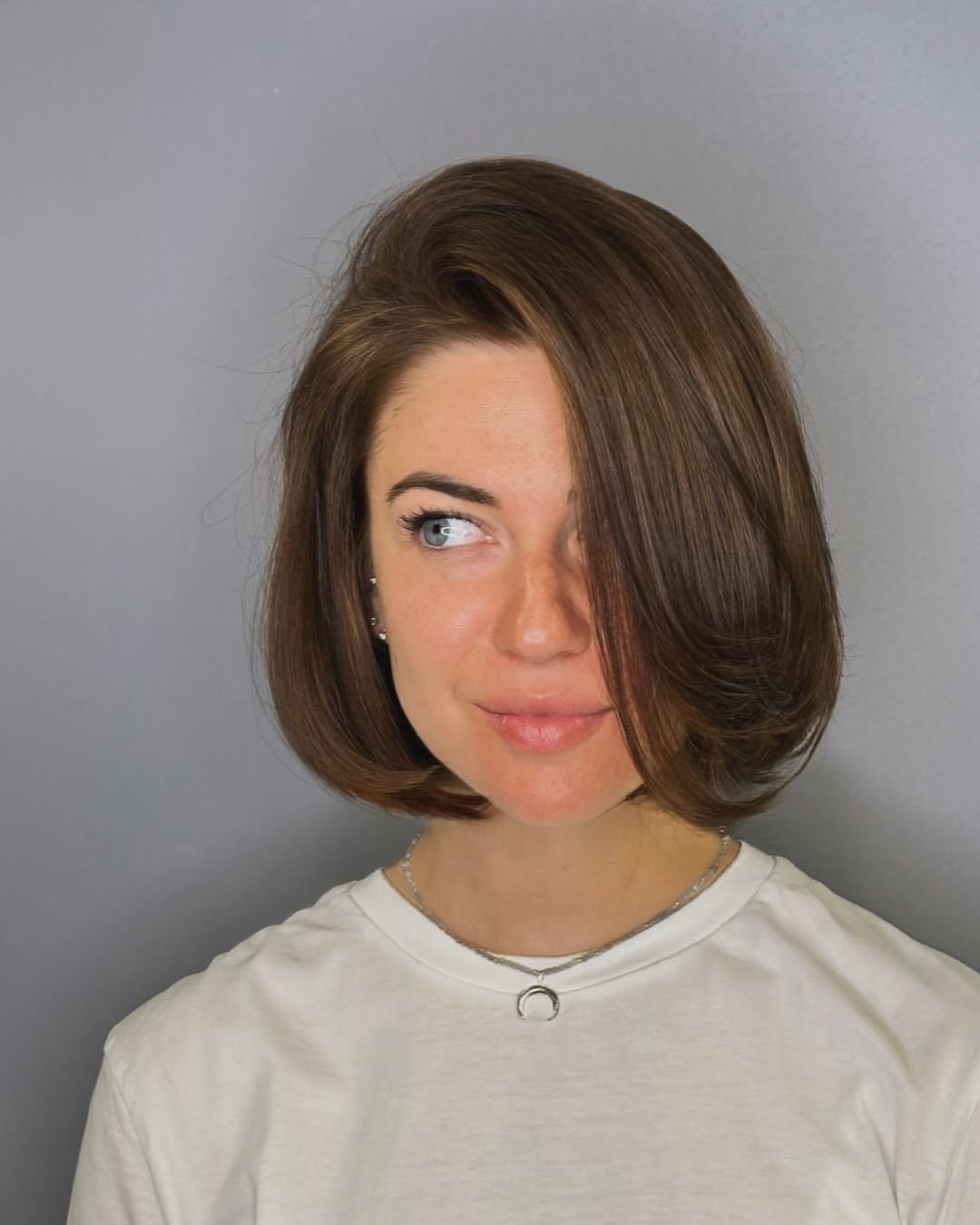 A woman confidently sporting a chic, shoulder-length bob haircut with subtle layers, perfect for women haircuts summer 2026. Her hair is a warm blonde, complementing her casual white linen top and hoop earrings.