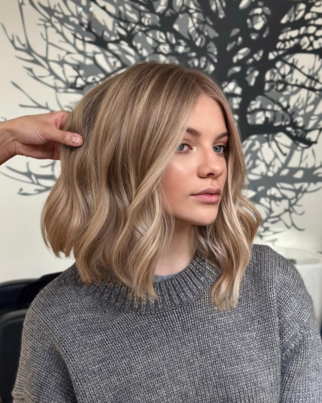 Close-up of a woman with a trendy shag haircut with bangs for summer 2026. Her hair is light brown with subtle highlights, framing her face perfectly.