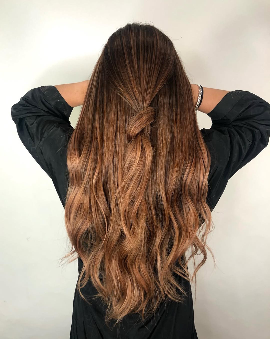 Radiant Caramel Brown Summer Hair 2026 Style A woman with radiant caramel brown summer hair 2026, styled in soft waves, wearing a white off-shoulder top and delicate gold jewelry, offering a sophisticated summery look.