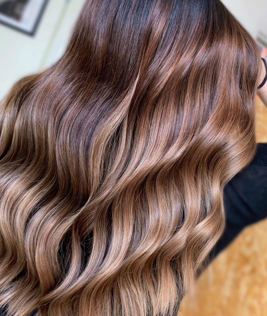Chic Caramel Brown Summer Hair Looks 2026 Woman with long, wavy caramel brown summer hair, wearing a white off-the-shoulder top and light wash jeans for a casual daytime look.