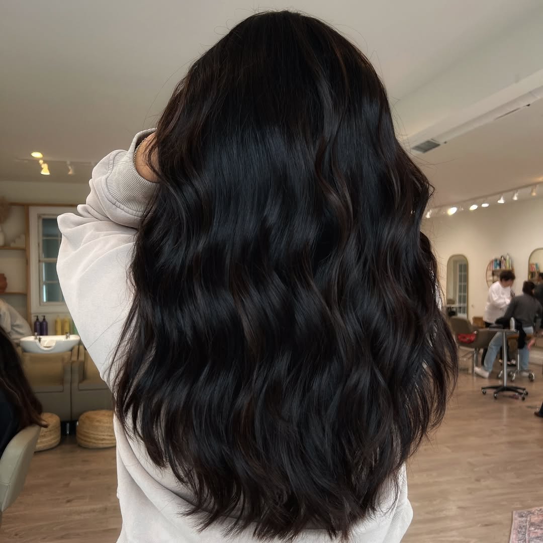 Edgy Dark Hair Summer 2026 Street Style Outfit A woman with edgy dark hair embraces the summer 2026 heat in a casual yet chic outfit: a black ribbed crop top paired with high-waisted distressed denim shorts and white sneakers, perfect for urban exploration.