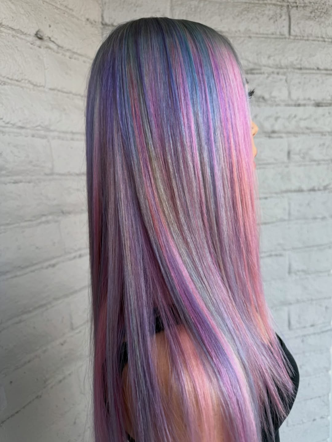 Woman with long, flowing pink and lavender pastel hair color for summer 2026, styled in casual waves, against a bright outdoor background.