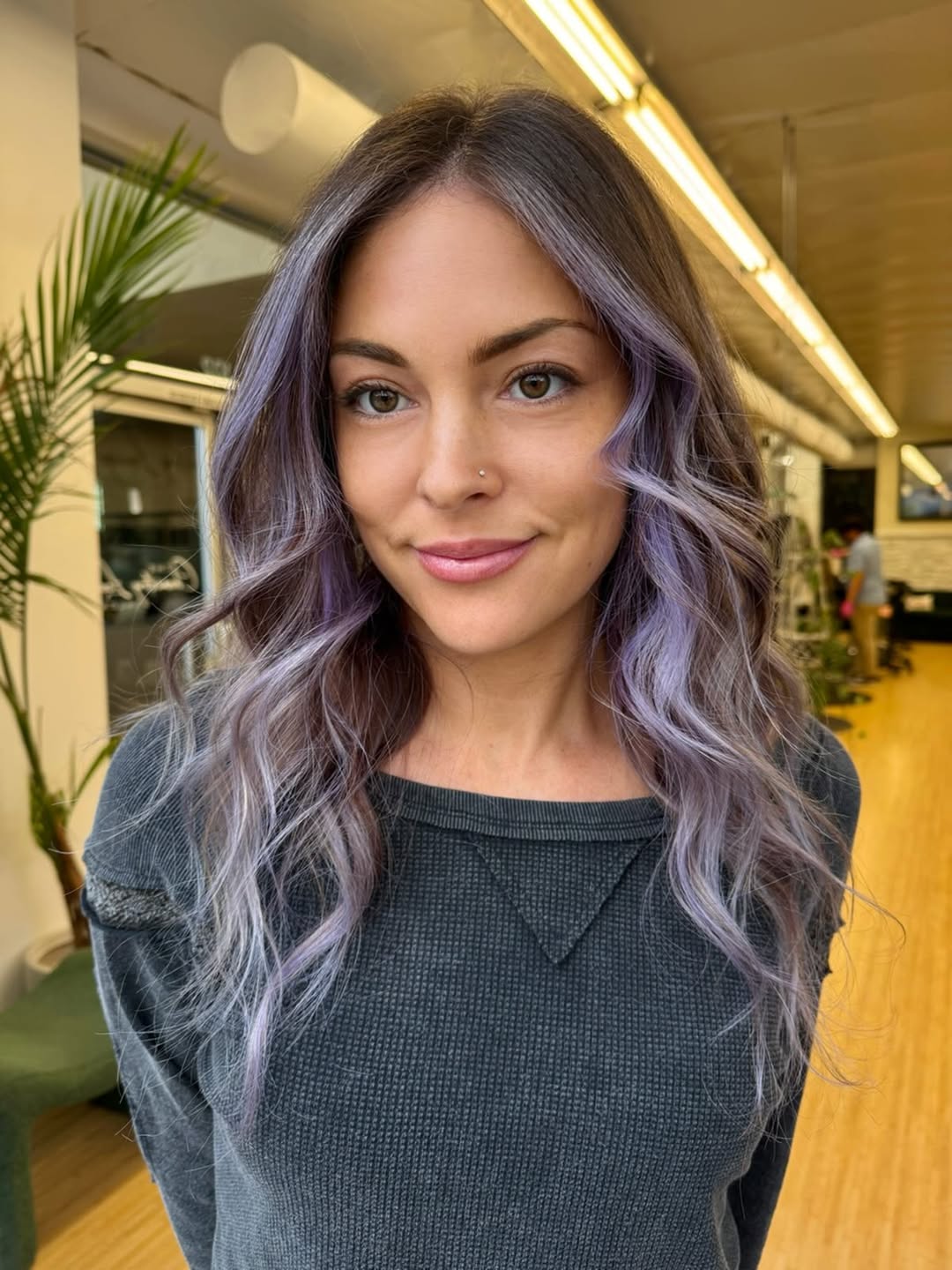Close-up of a woman with vibrant pastel pink and purple hair, styled in loose waves, perfect for pastel hair color summer 2026 trends. She's wearing a delicate floral top.