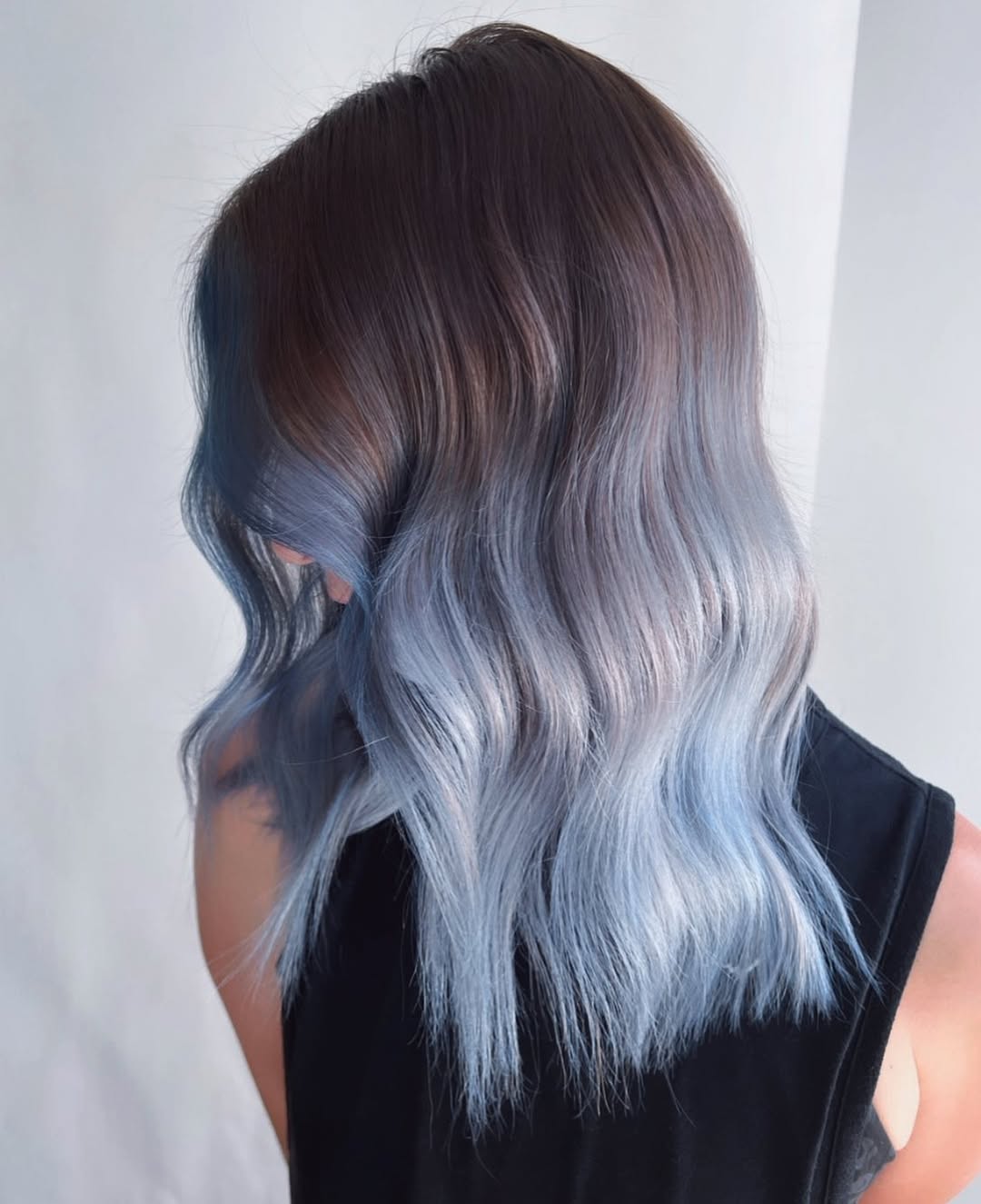 Woman with long, wavy pastel pink and purple hair, wearing a white off-the-shoulder top and denim shorts, enjoying a sunny summer day. Perfect for pastel hair color summer 2026 inspiration.