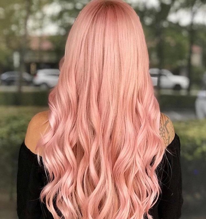 A young woman smiling, showcasing long, wavy hair dyed in various pastel shades including lilac, rose, and sky blue, a perfect pastel hair color for summer 2026. She wears a simple white top, highlighting the vibrant hair.