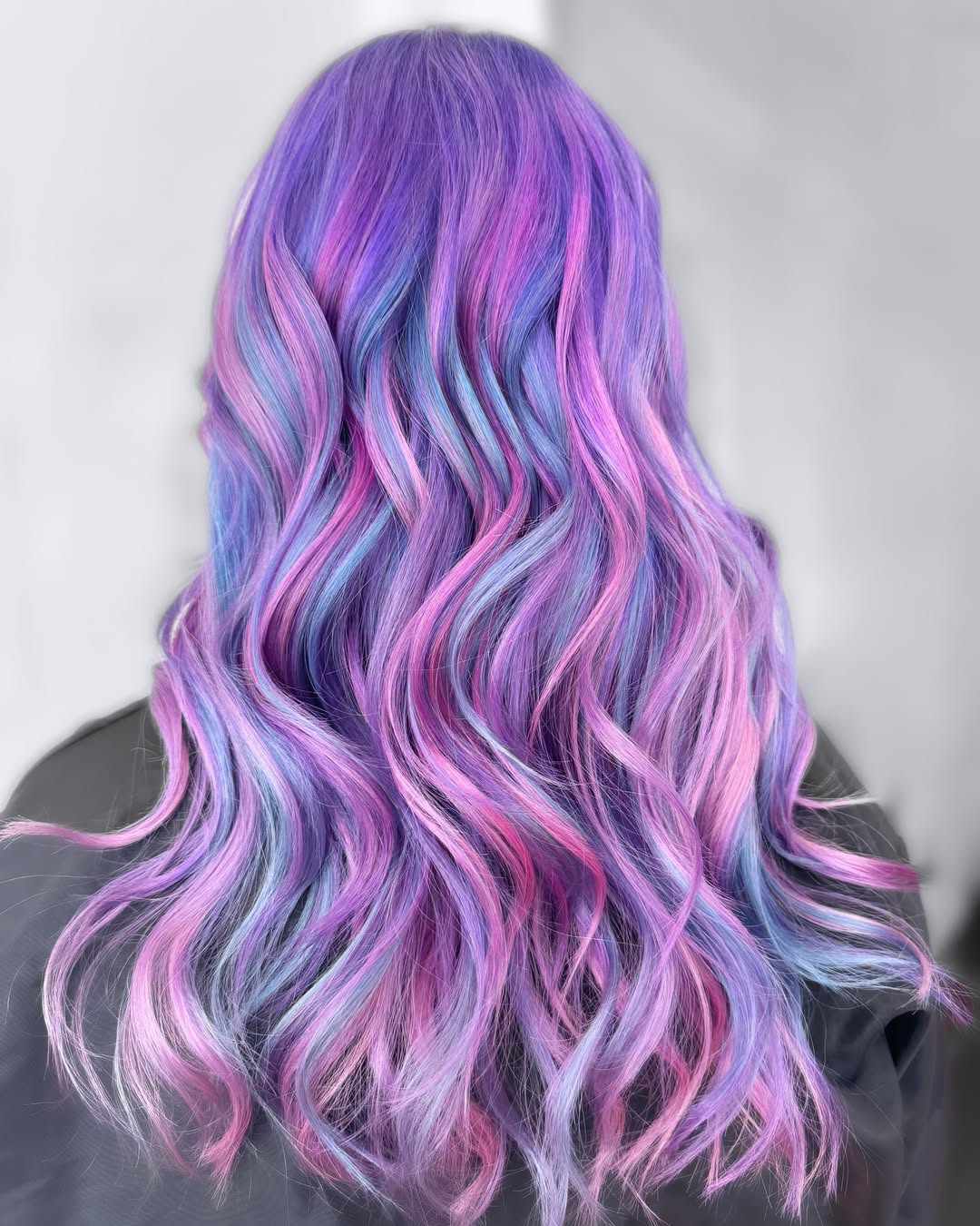 Close-up of a woman with vibrant pastel pink hair, styled in loose waves, enjoying a sunny summer day. Perfect for pastel hair color summer 2026 inspiration.