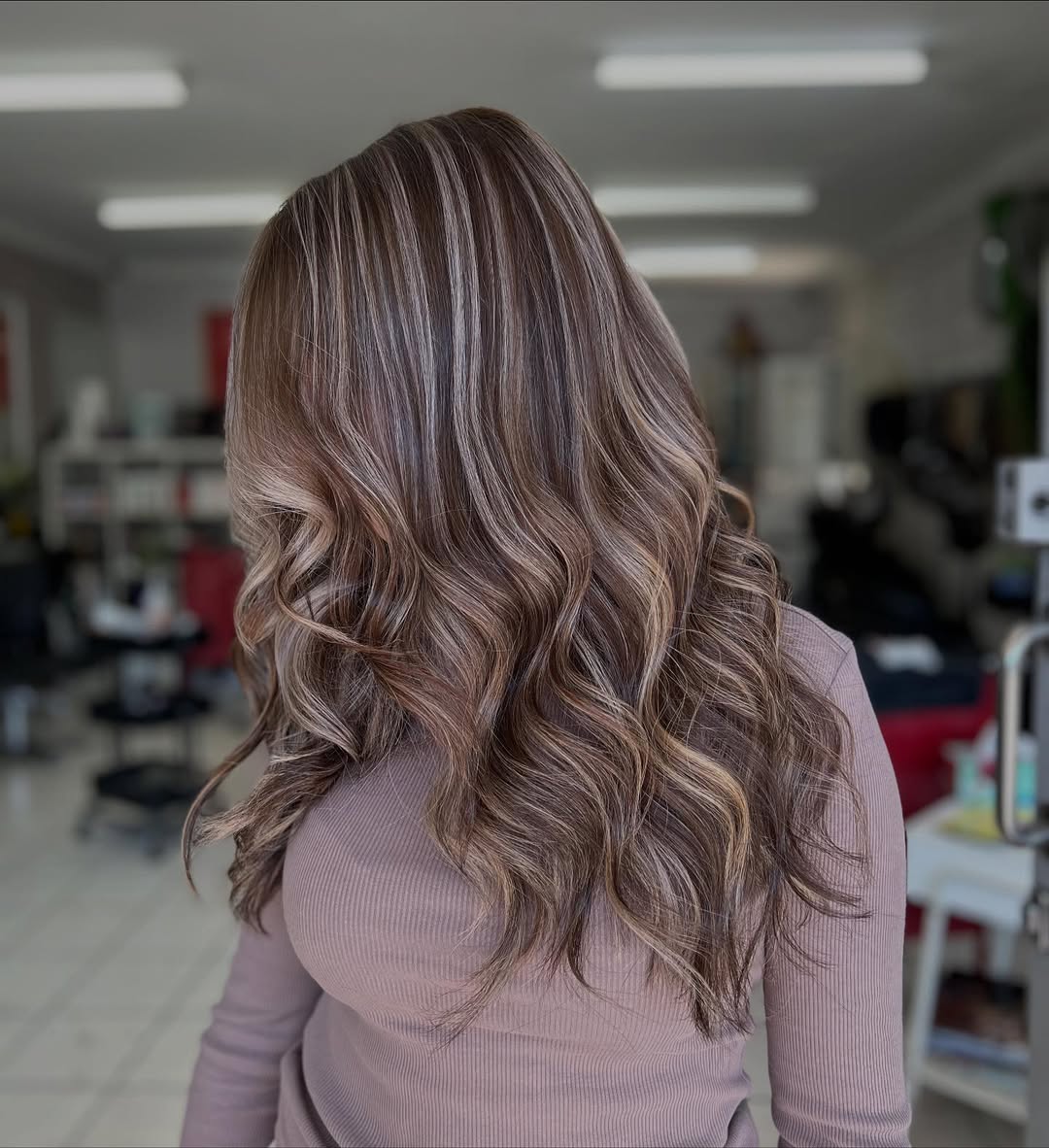 A woman with beautiful subtle highlights summer hair 2026, light brown with sun-kissed blonde streaks, smiling brightly outdoors.