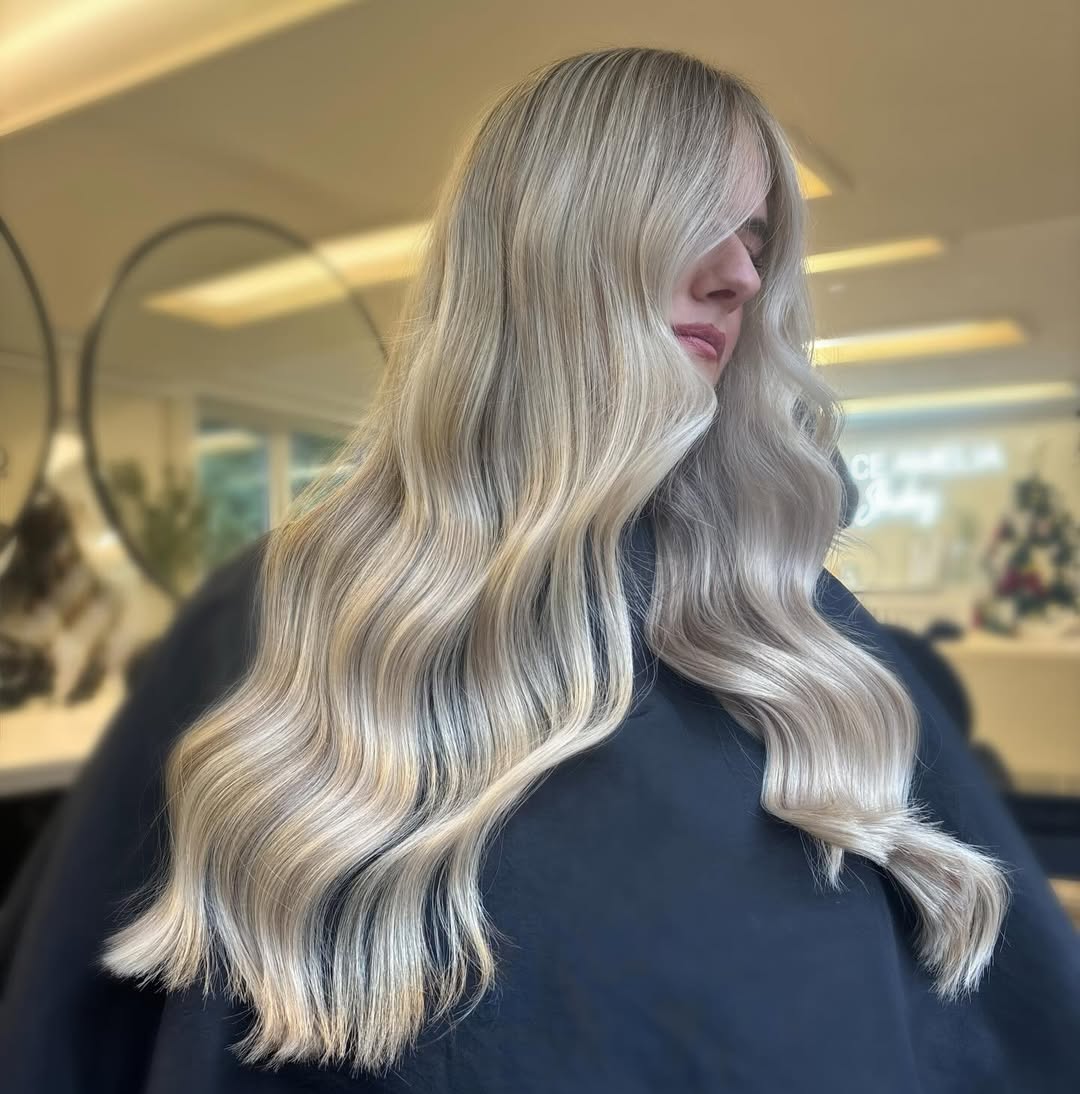 Woman with long, wavy brown hair featuring gorgeous subtle highlights, ideal for summer 2026. Her hair has light caramel tones around her face and ends, styled casually for a natural summery look.
