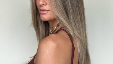 A woman smiles, showcasing vibrant copper summer hair color cute ideas 2026, styled in soft waves perfect for beach days or casual outings. Her sun-kissed skin and tank top complement the warm tones.
