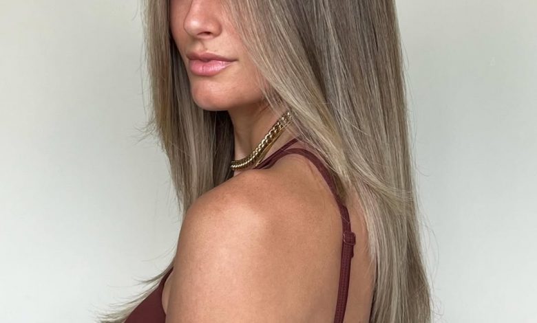 A woman smiles, showcasing vibrant copper summer hair color cute ideas 2026, styled in soft waves perfect for beach days or casual outings. Her sun-kissed skin and tank top complement the warm tones.