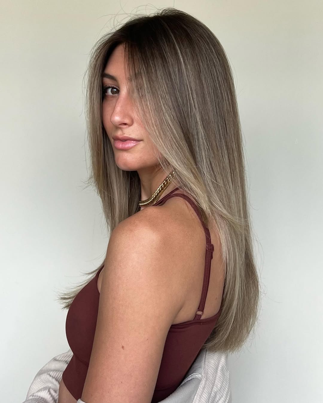 A woman smiles, showcasing vibrant copper summer hair color cute ideas 2026, styled in soft waves perfect for beach days or casual outings. Her sun-kissed skin and tank top complement the warm tones.
