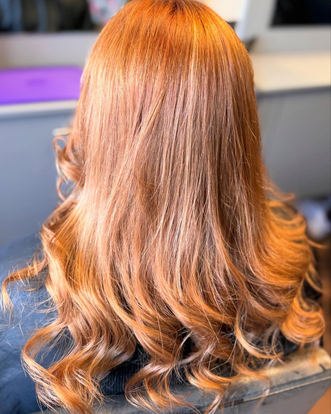 Close-up of a woman with vibrant copper-red hair styled in loose waves, showcasing a beautiful summer hair color cute idea. Her hair glows in the sun, perfect for a warm weather look.