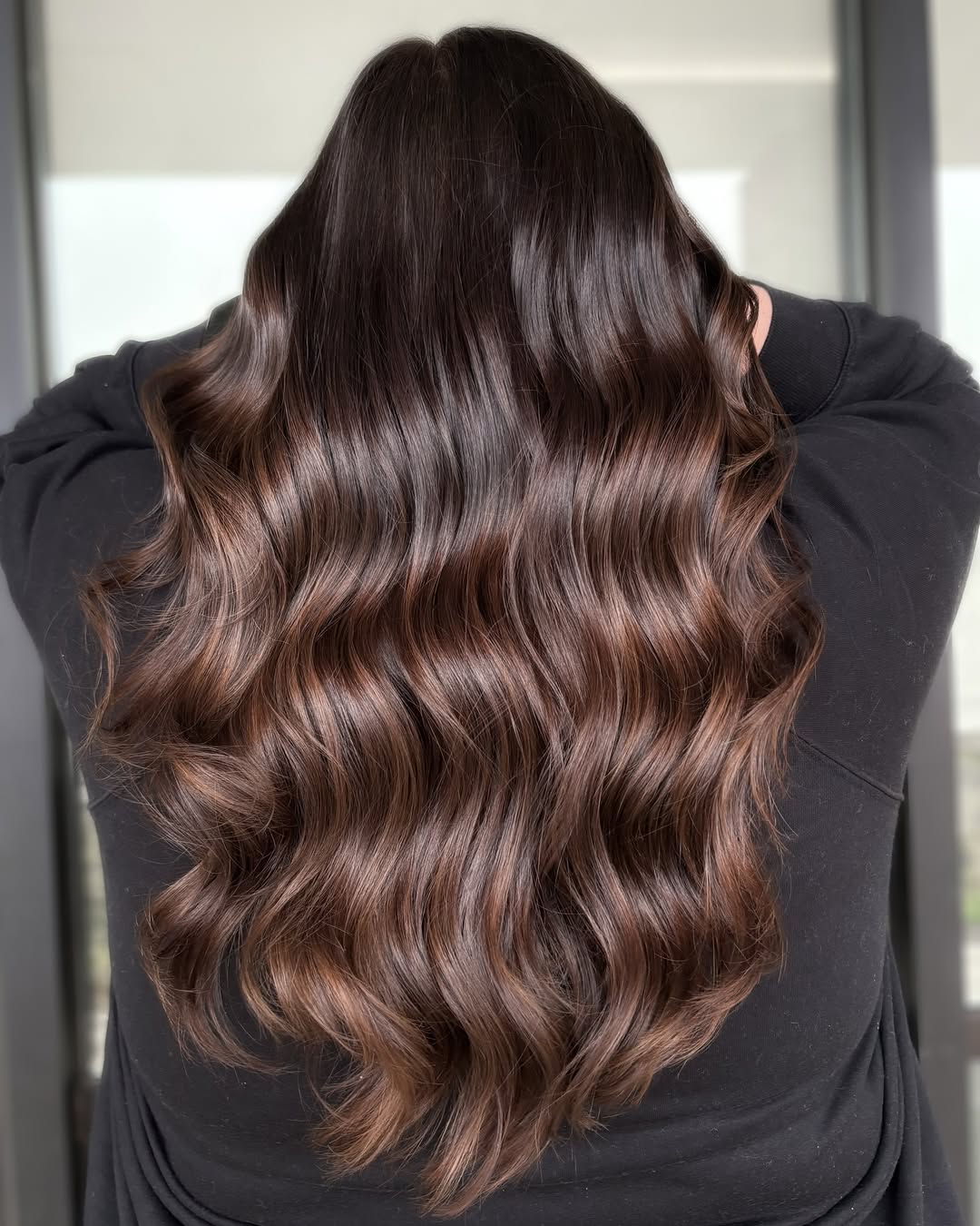 Stunning Wavy Summer Hair for Brunettes 2026 Close-up of a smiling brunette woman with long, sun-kissed wavy hair, perfect for summer hair for brunettes 2026. Her hair has subtle golden highlights catching the light, framing her face beautifully, ideal for a casual daytime look.