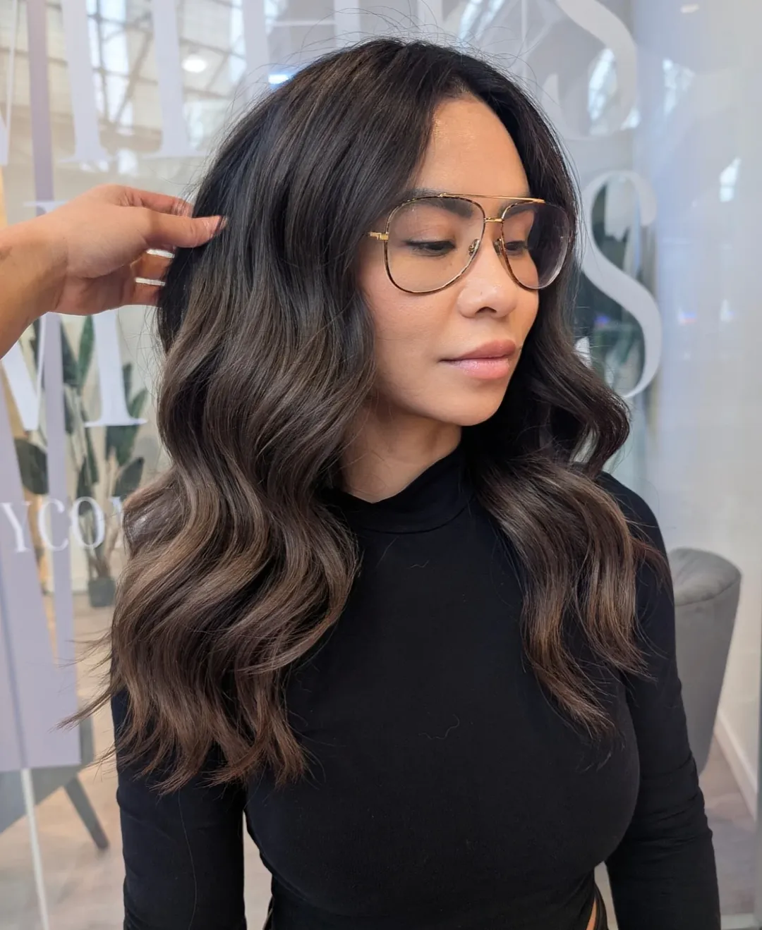 Stunning Wavy Summer Hair for Brunettes 2026 Close-up of a brunette woman with long, shiny, wavy hair framing her face, styled for summer. Her hair has subtle golden highlights, perfect for summer hair for brunettes 2026. She is smiling softly, suggesting a natural and effortless look.