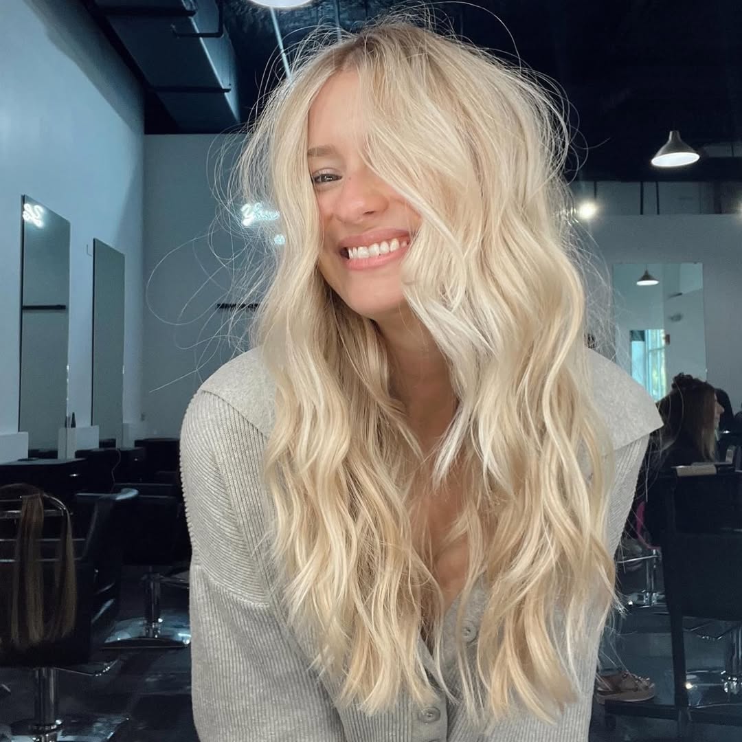 A woman confidently smiles, showcasing soft, sun-kissed waves adorned with a delicate floral headband, perfect for chic summer hair ideas women 2026.