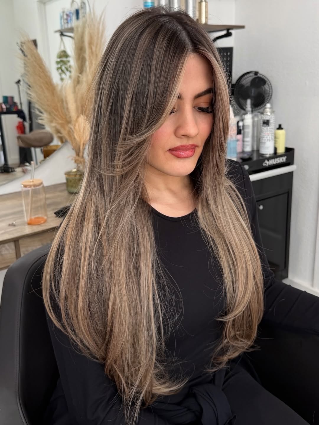 A woman with vibrant blonde balayage long wavy hair, showcasing perfect summer hair ideas for women. Her hair is effortlessly styled, catching the light beautifully for a chic look.
