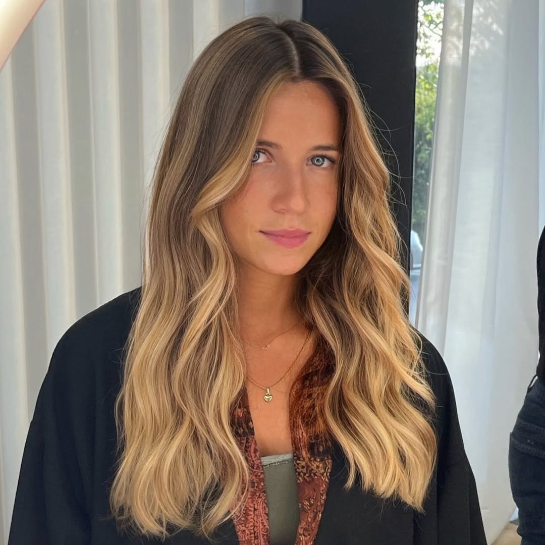 Beautiful woman with long, sun-kissed blonde hair styled in soft waves; perfect summer hair ideas for women 2026. She wears a white lace top, ideal for a beach vacation or casual outdoor event.