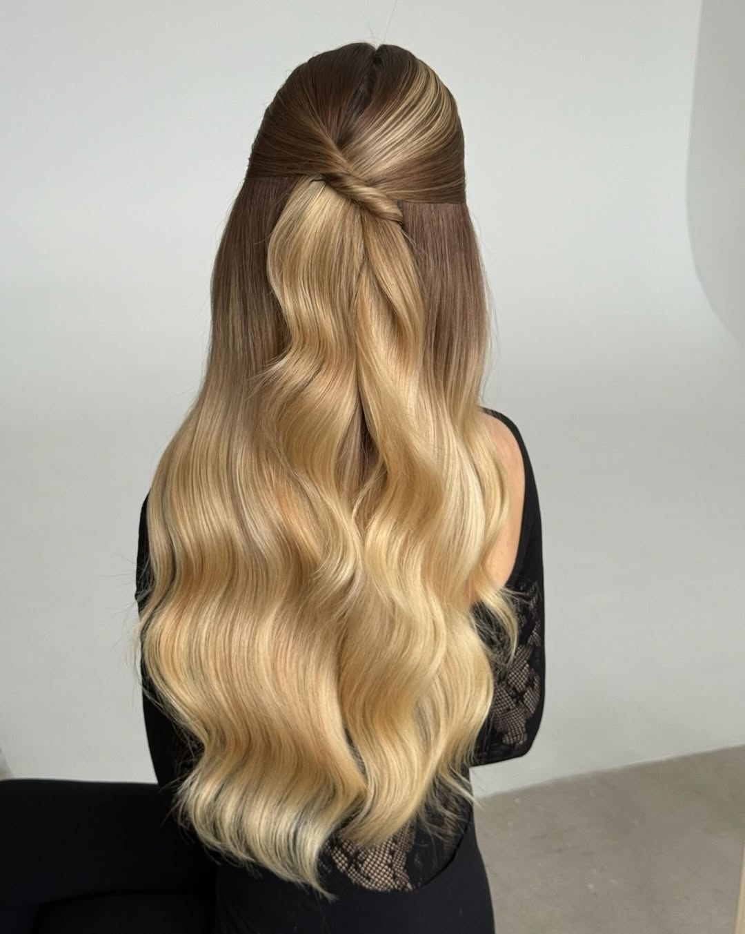 Woman with long, wavy blonde hair styled in a half-updo with face-framing pieces, perfect for summer hairstyles long hair ideas 2026. She wears a flowy white dress in a sunny outdoor setting.