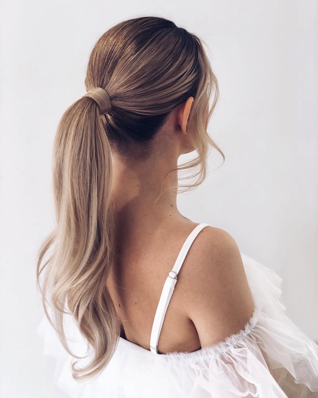 Woman with long, wavy blonde hair styled in a half-up twist, perfect for summer hairstyles long hair ideas 2026. Her hair is casually elegant, showcasing sun-kissed highlights.